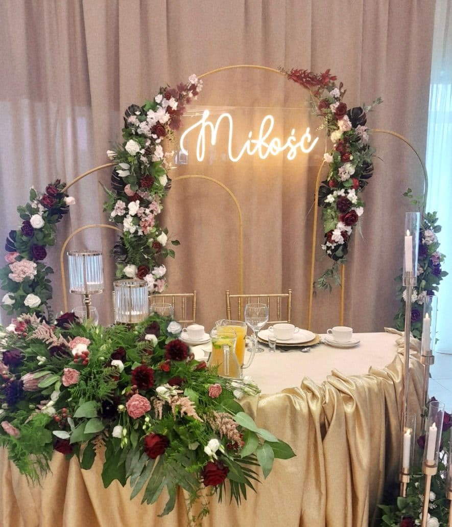 Stół ubrany na wesele z napisem Miłość i aranżacjami z kwiatów, złoty obrus z nakryciem